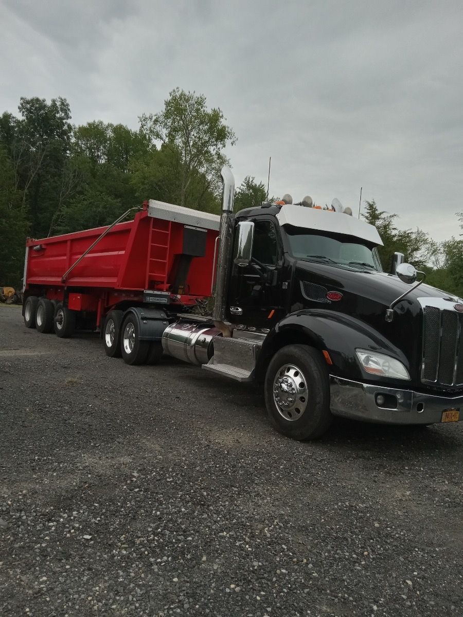 A black semi truck with a red dump trailer attached to it