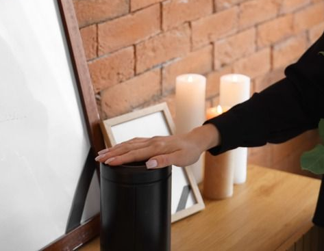 A person's hand rests on a black cylinder next to candles and a mirror. Brick wall in background.