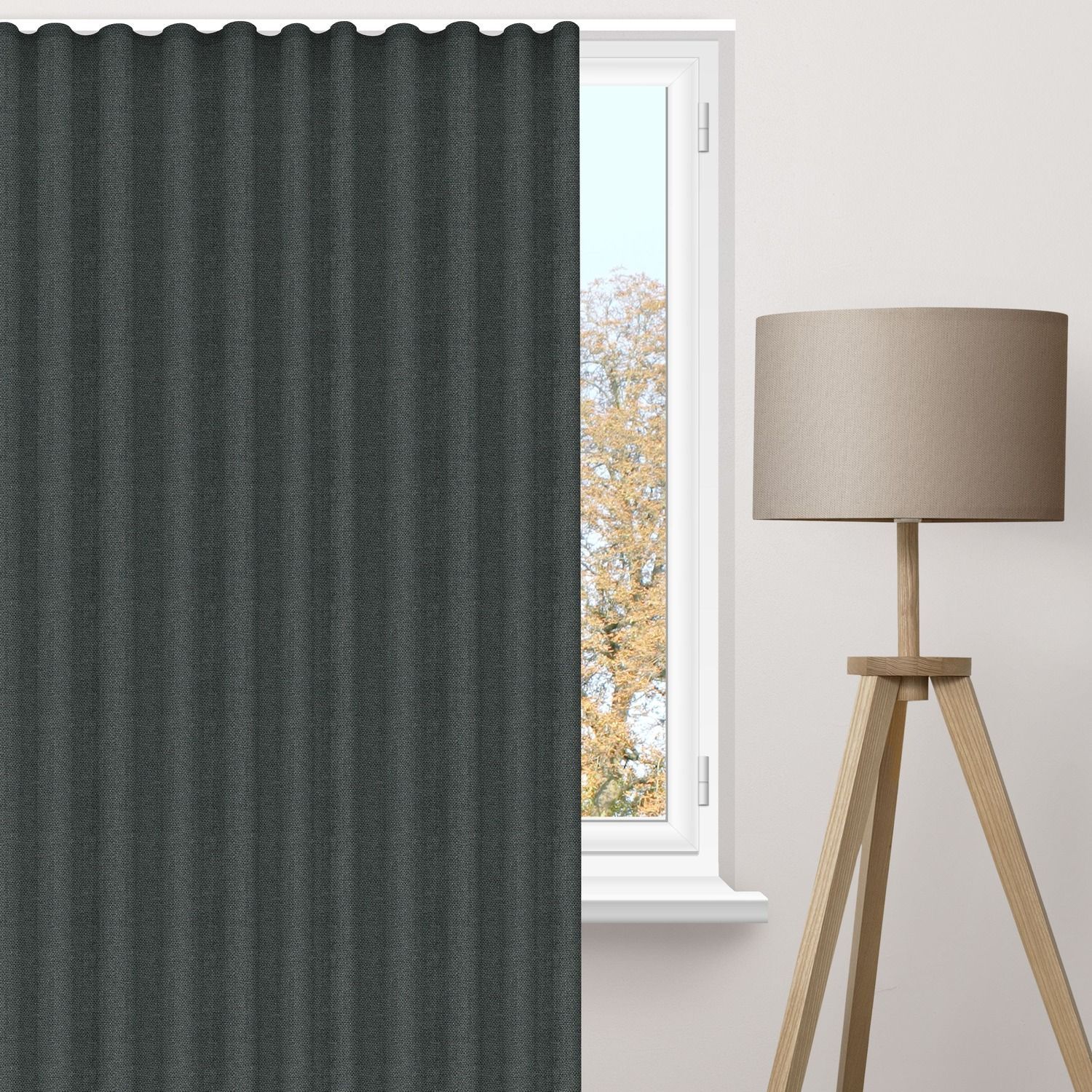 Blackout curtains covering half a window beside a modern tripod lamp, showing how blackout curtains enhance privacy and block natural light effectively.