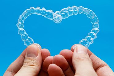 Hands holding dental aligners in heart shape on blue background