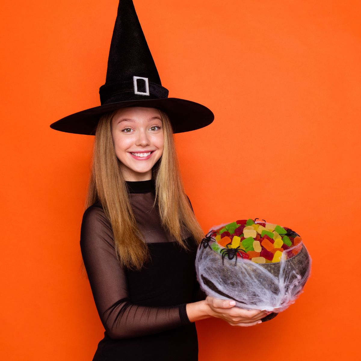 A woman in a witch costume is holding a bowl of candy.