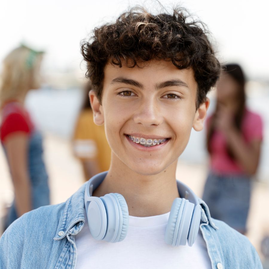 A young man with braces and headphones around his neck is smiling.