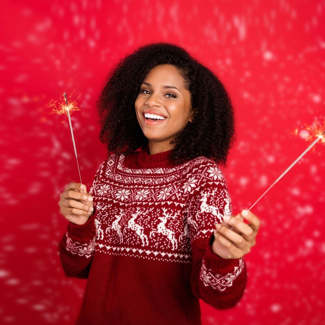 A woman in a red sweater is holding sparklers in her hands.