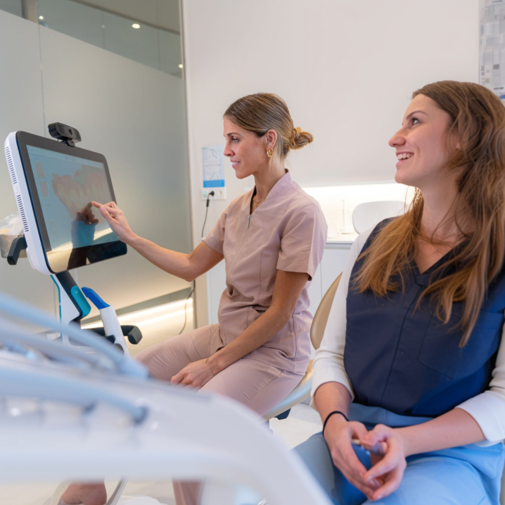Two women are sitting in a dental chair looking at a computer screen.