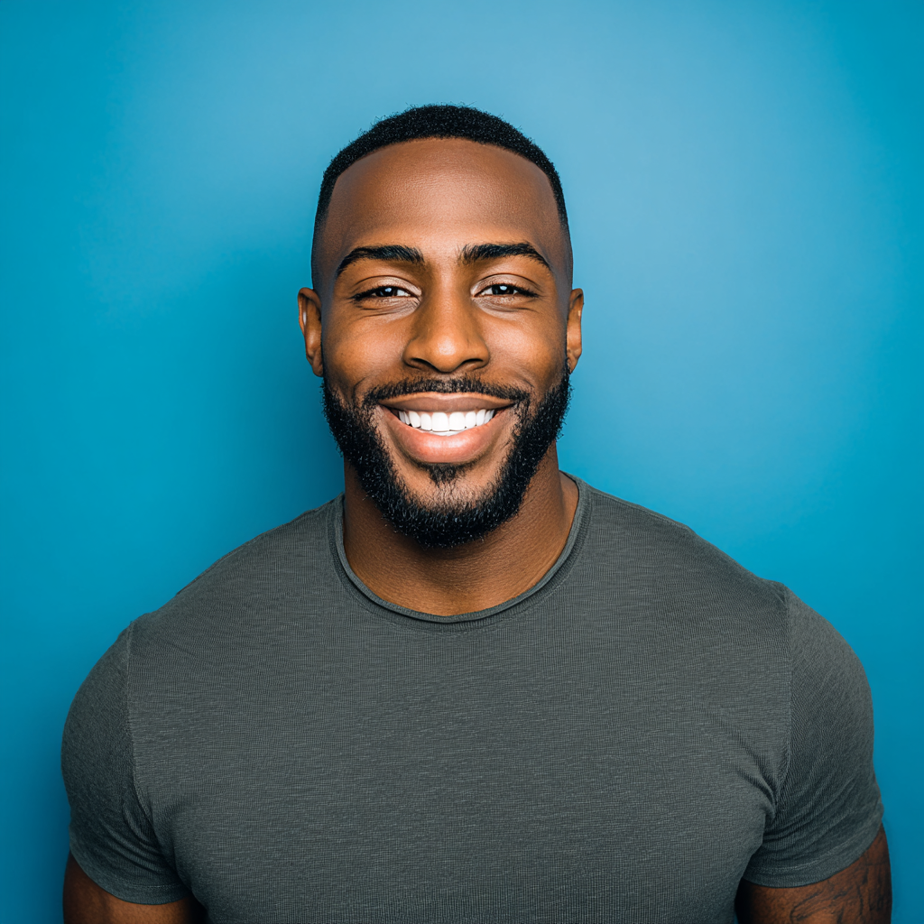 Man with dark skin smiling, wearing a gray shirt, against a blue background.