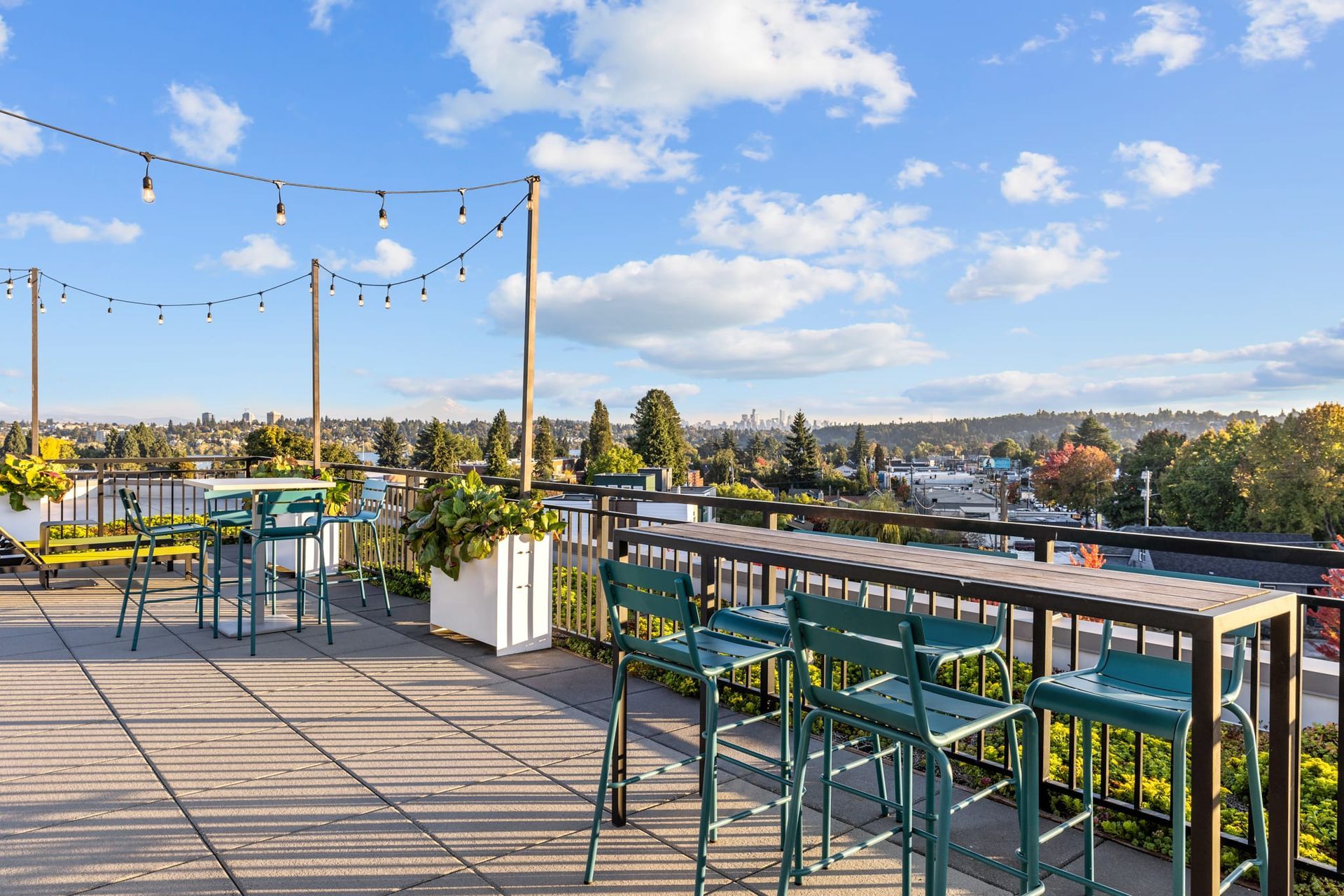 A rooftop deck with tables and chairs and a view of the city at CREW Apartments in Seattle, WA.