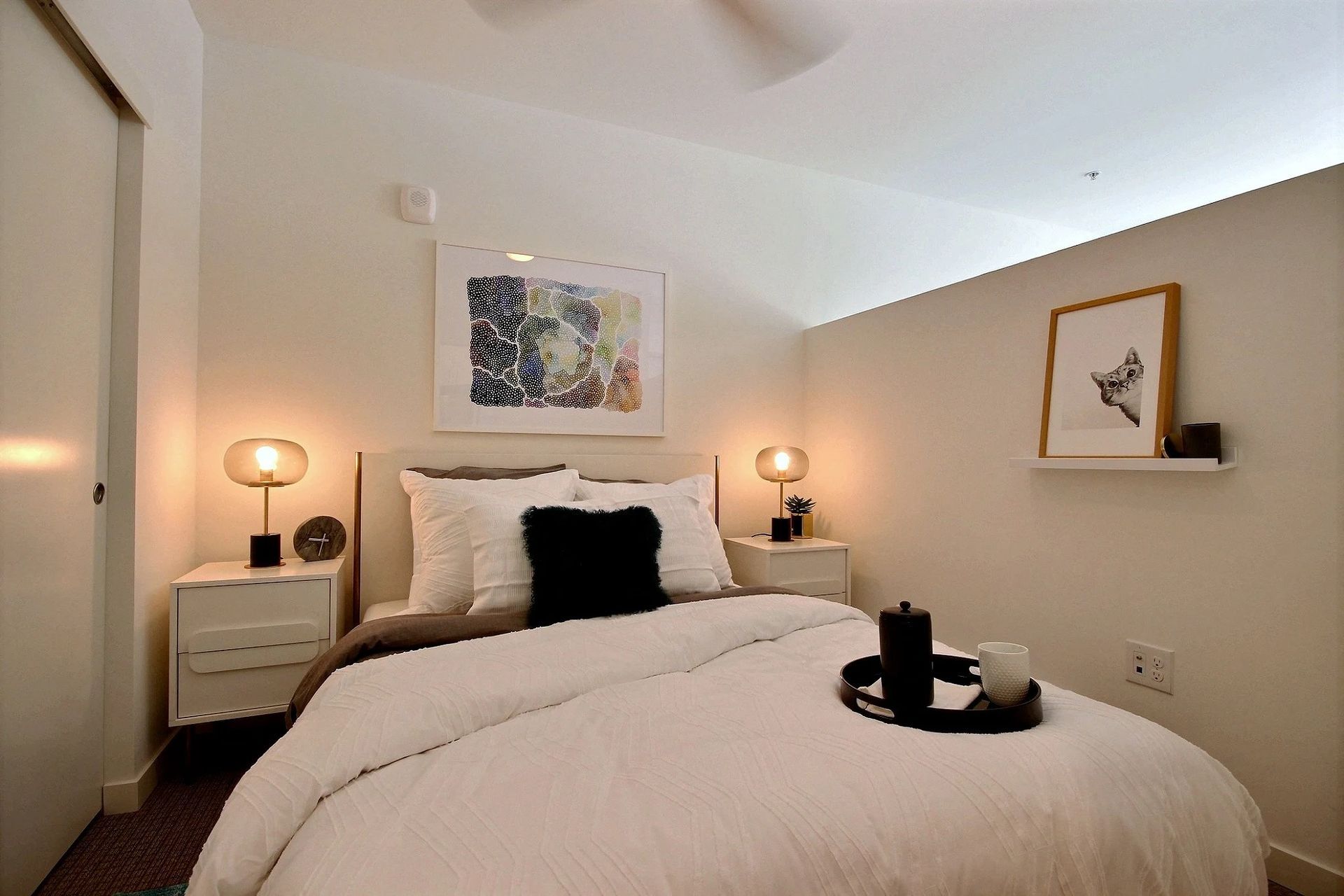 A bedroom with a bed , nightstands , lamps and a picture on the wall at CREW Apartments in Seattle, WA.