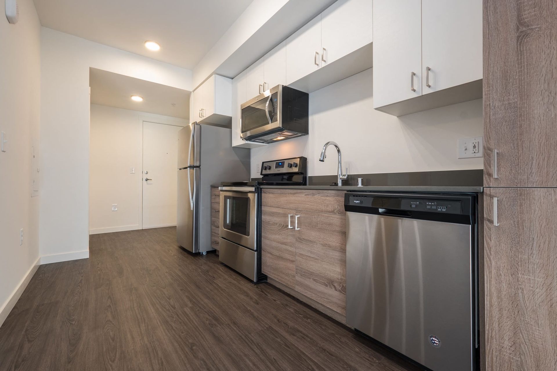 A kitchen with stainless steel appliances and wooden cabinets at CREW Apartments in Seattle, WA.