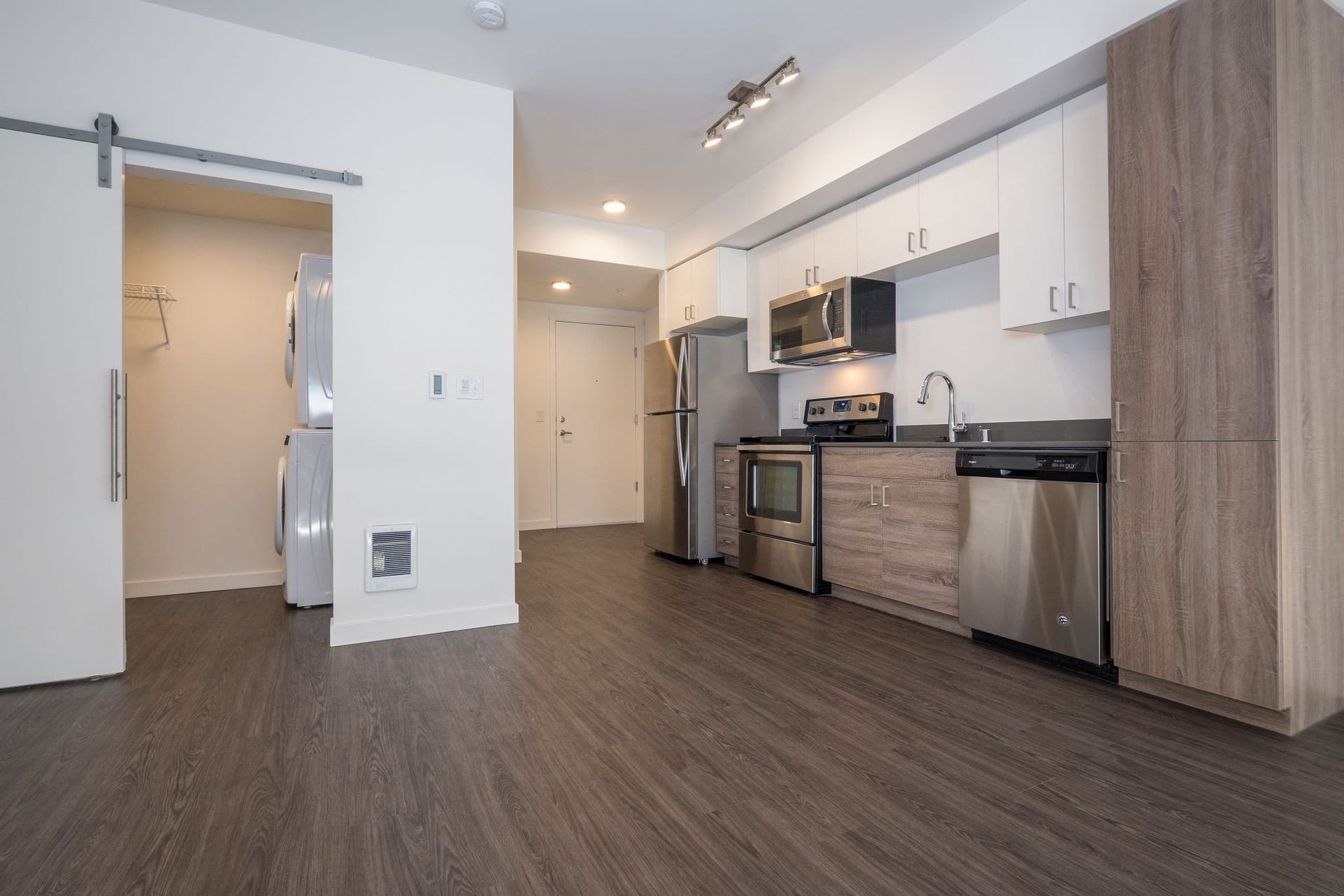 A kitchen with stainless steel appliances , wooden cabinets and a sliding barn door at CREW Apartments in Seattle, WA.