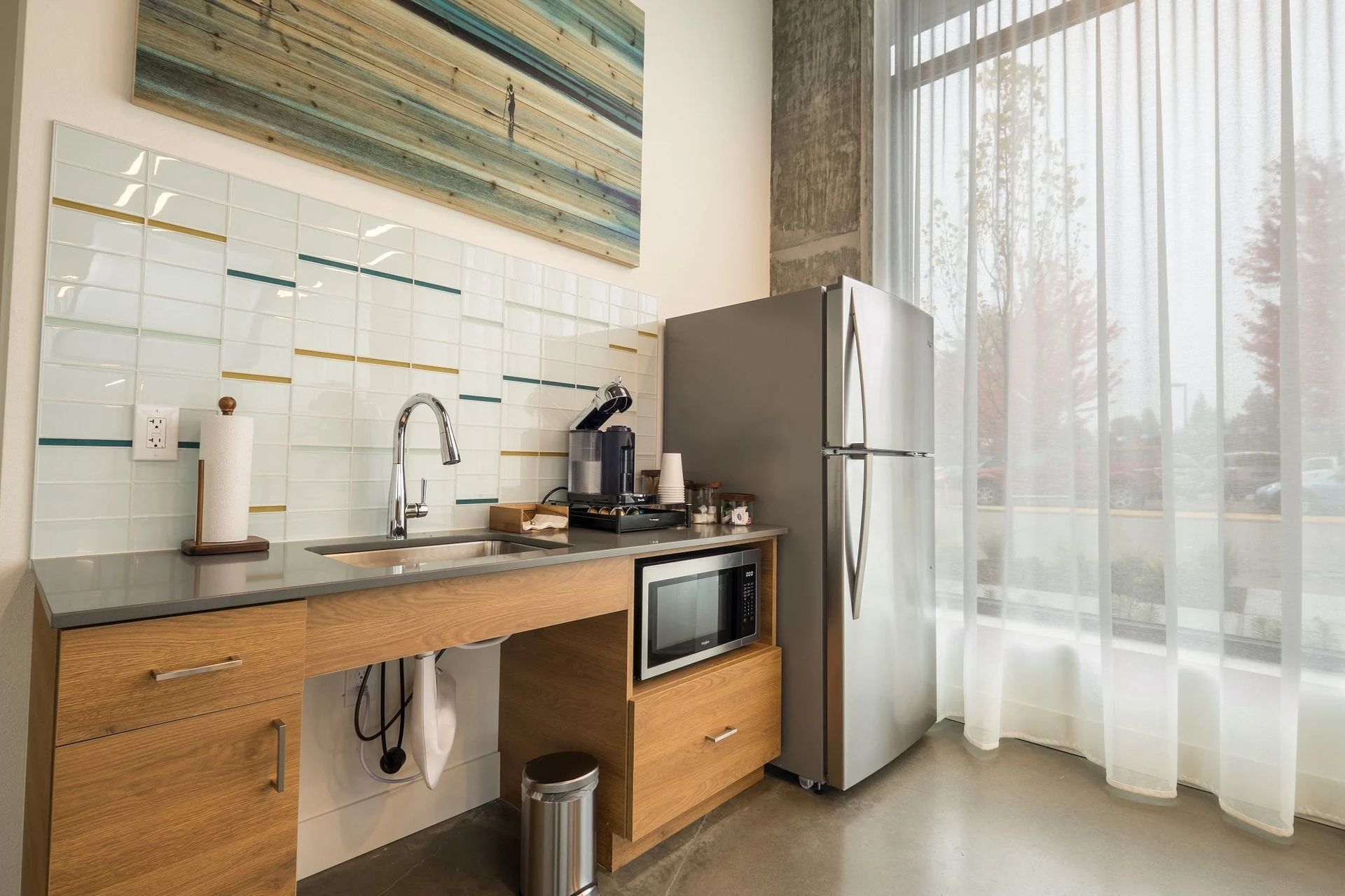 A kitchen with a sink , refrigerator , microwave and a large window at CREW Apartments in Seattle, WA.