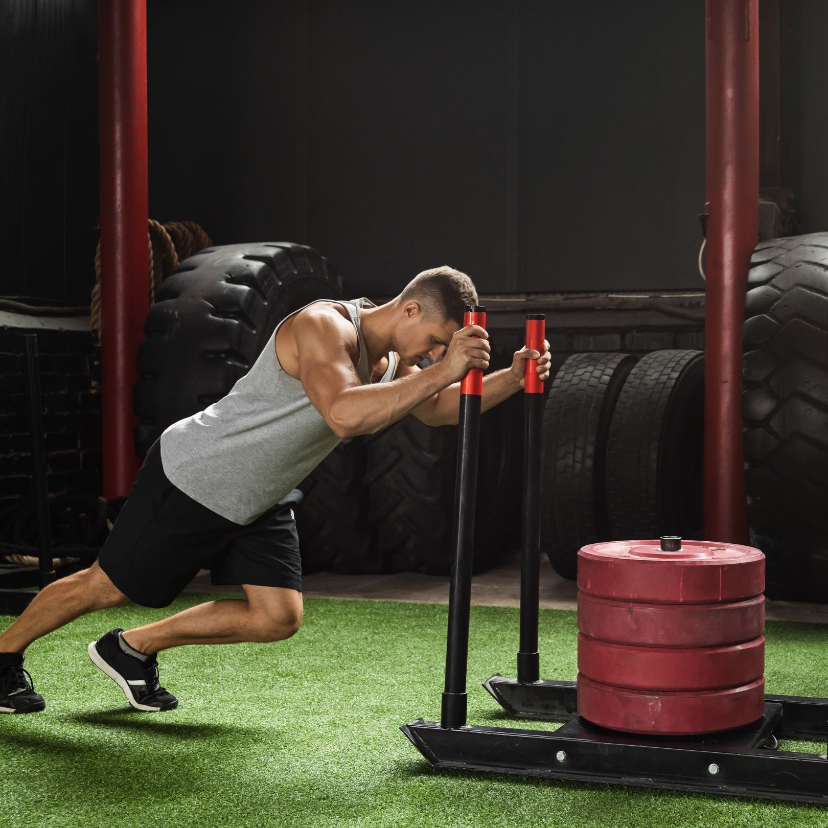 A person pushes a weighted sled across a gym's turf surface.