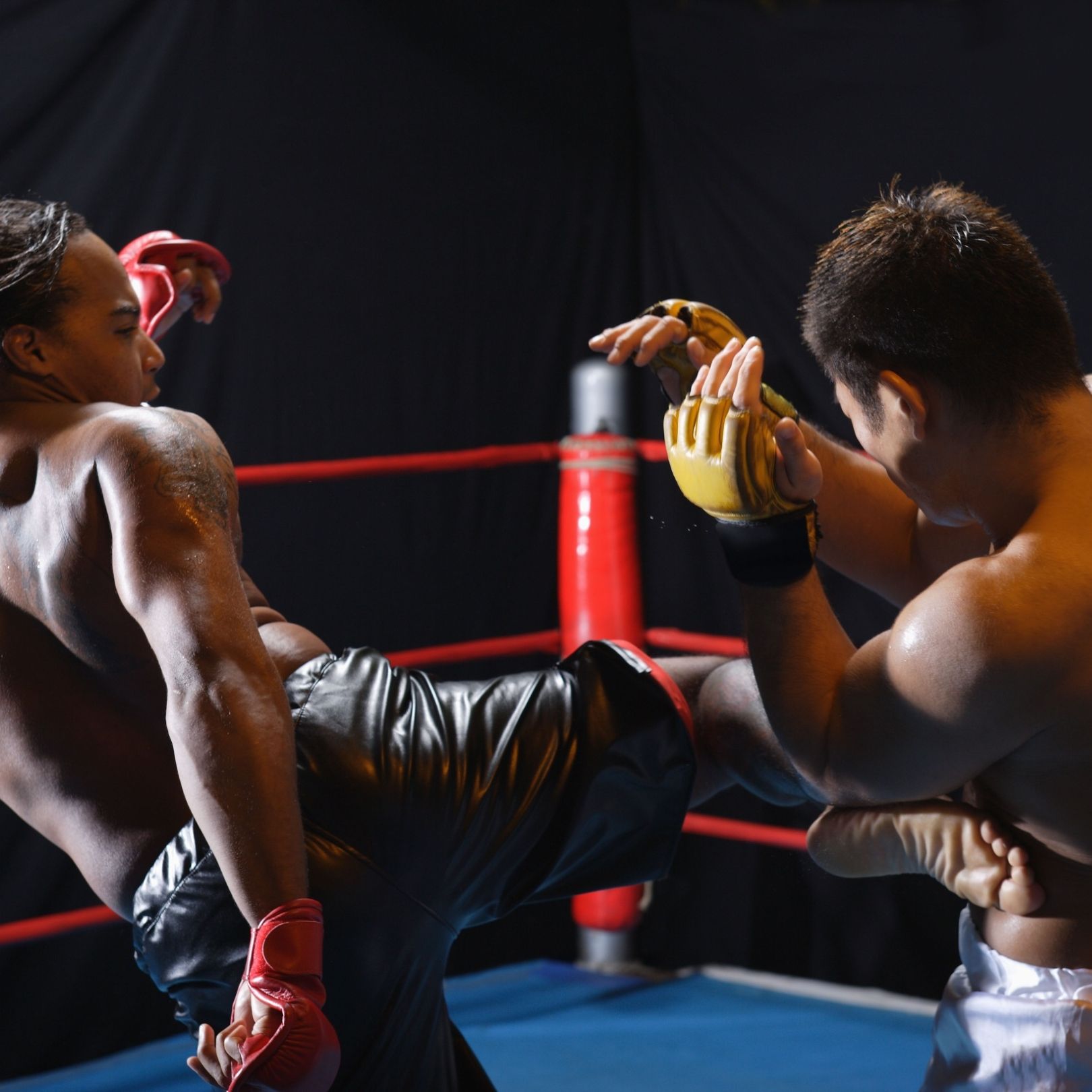 Two martial artists in a boxing ring, one throwing a leg kick blocked by the other's arms.