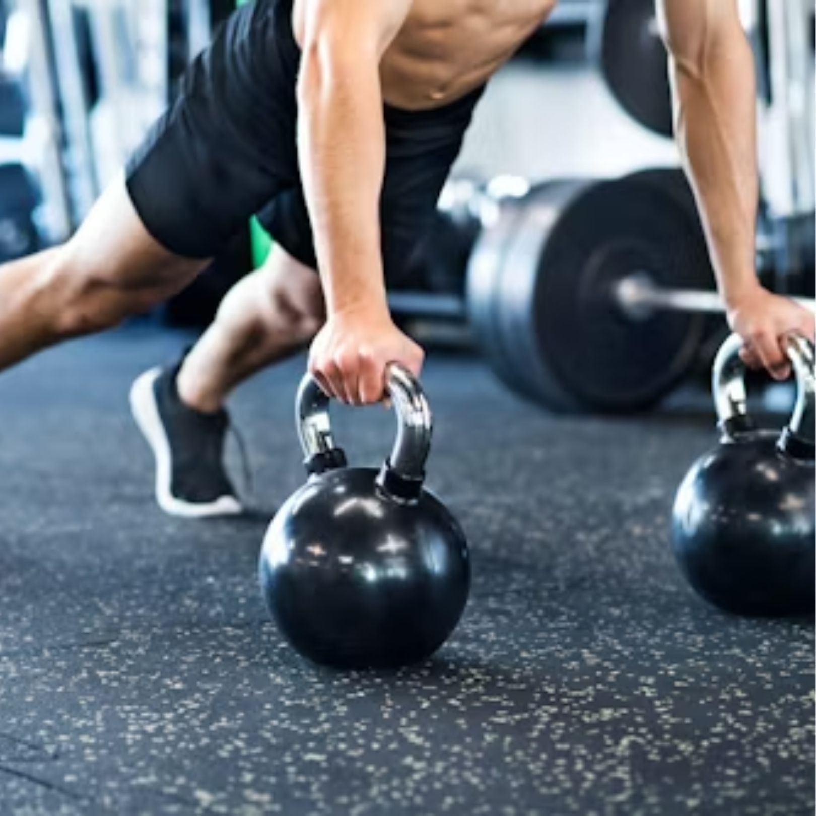 A person in a gym performing renegade rows, holding onto two black kettlebells while in a plank position.