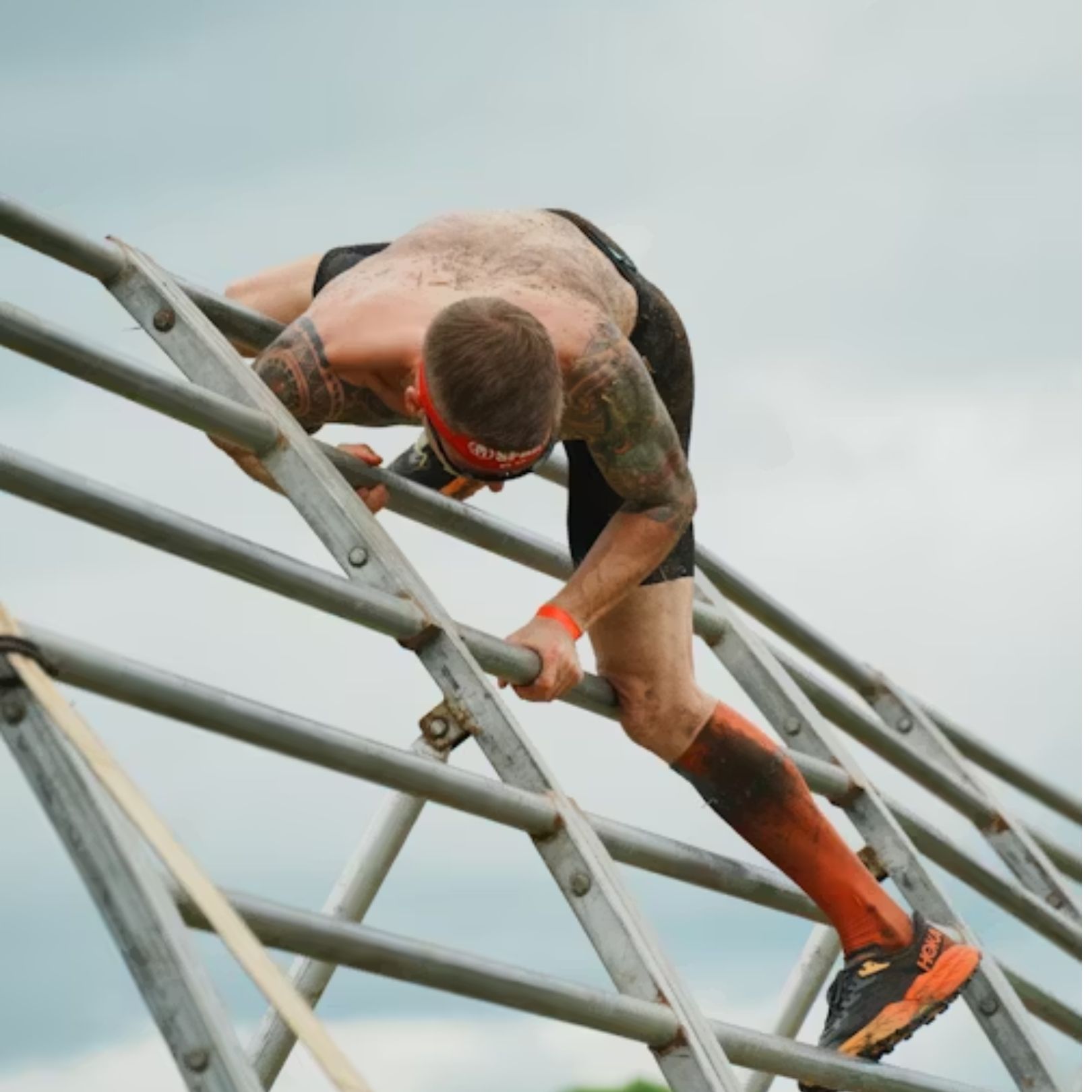 A person with tattoos climbs a metal A-frame obstacle in an outdoor obstacle course race.