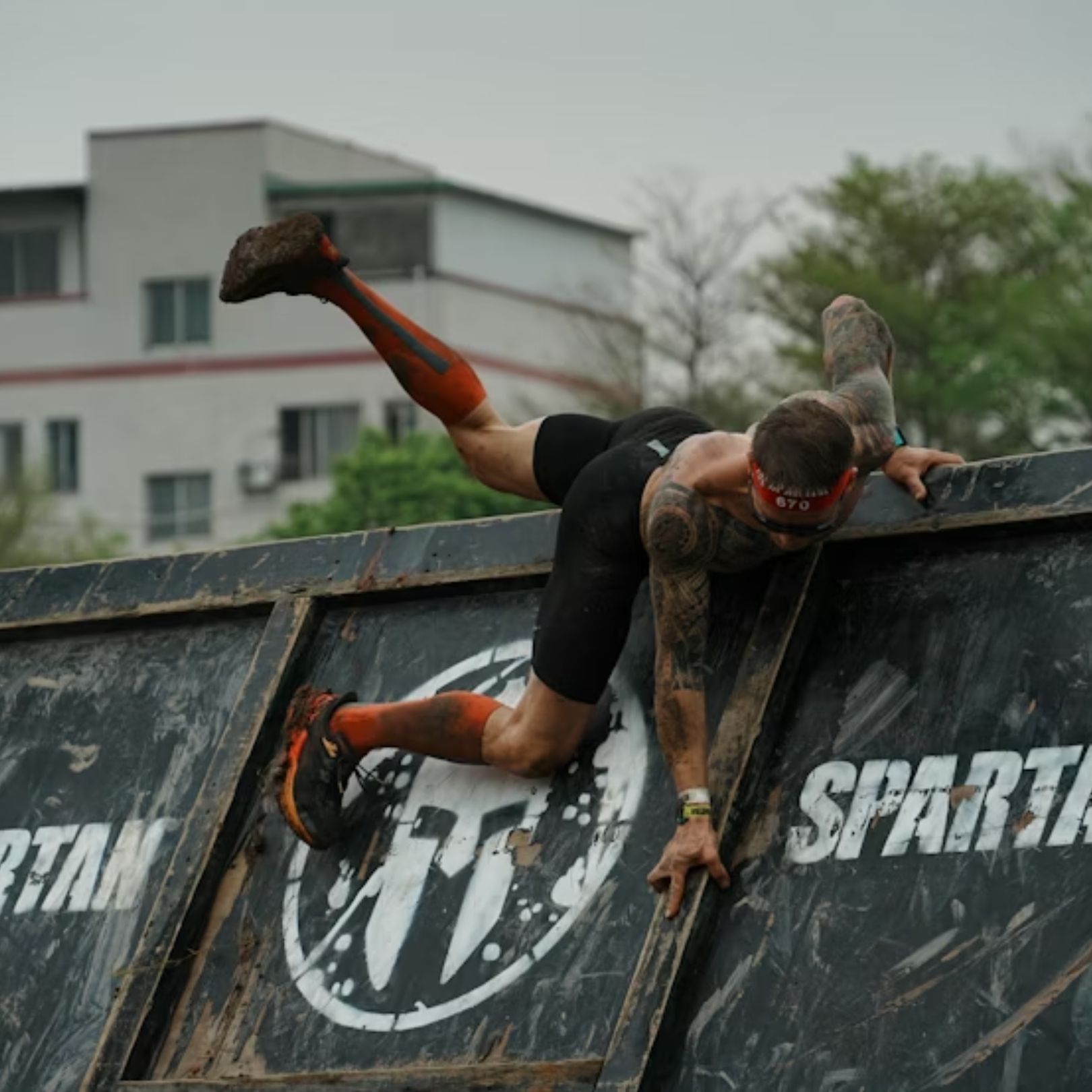 A participant climbs over a black, Spartan-branded wall during an outdoor obstacle race.