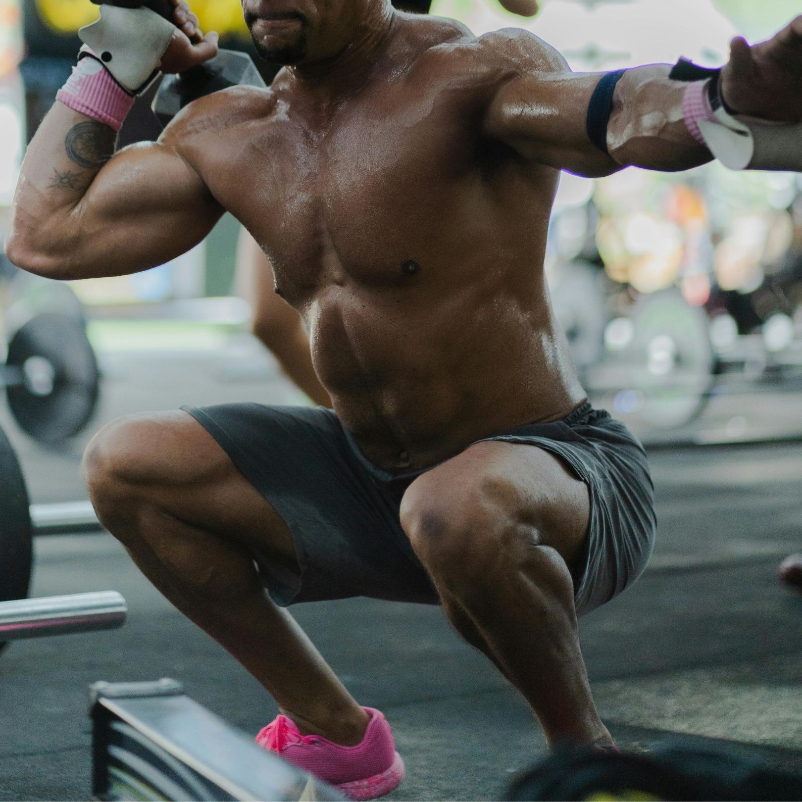 A muscular person performing a deep squat in a gym, wearing workout clothes and pink sneakers.