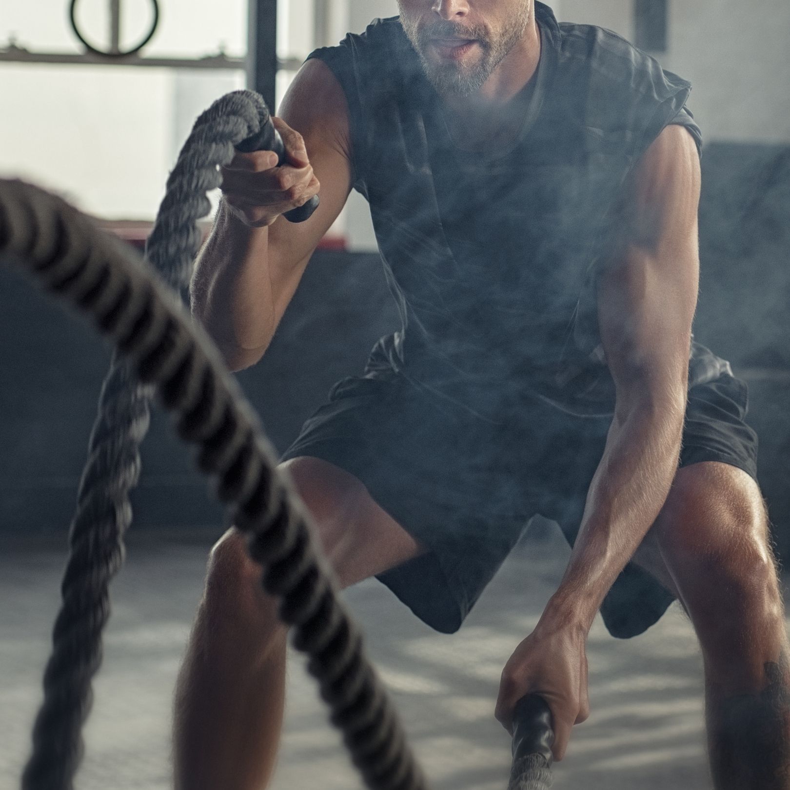 A person in a gym performing a high-intensity battle rope workout, creating a cloud of dust while holding heavy ropes.
