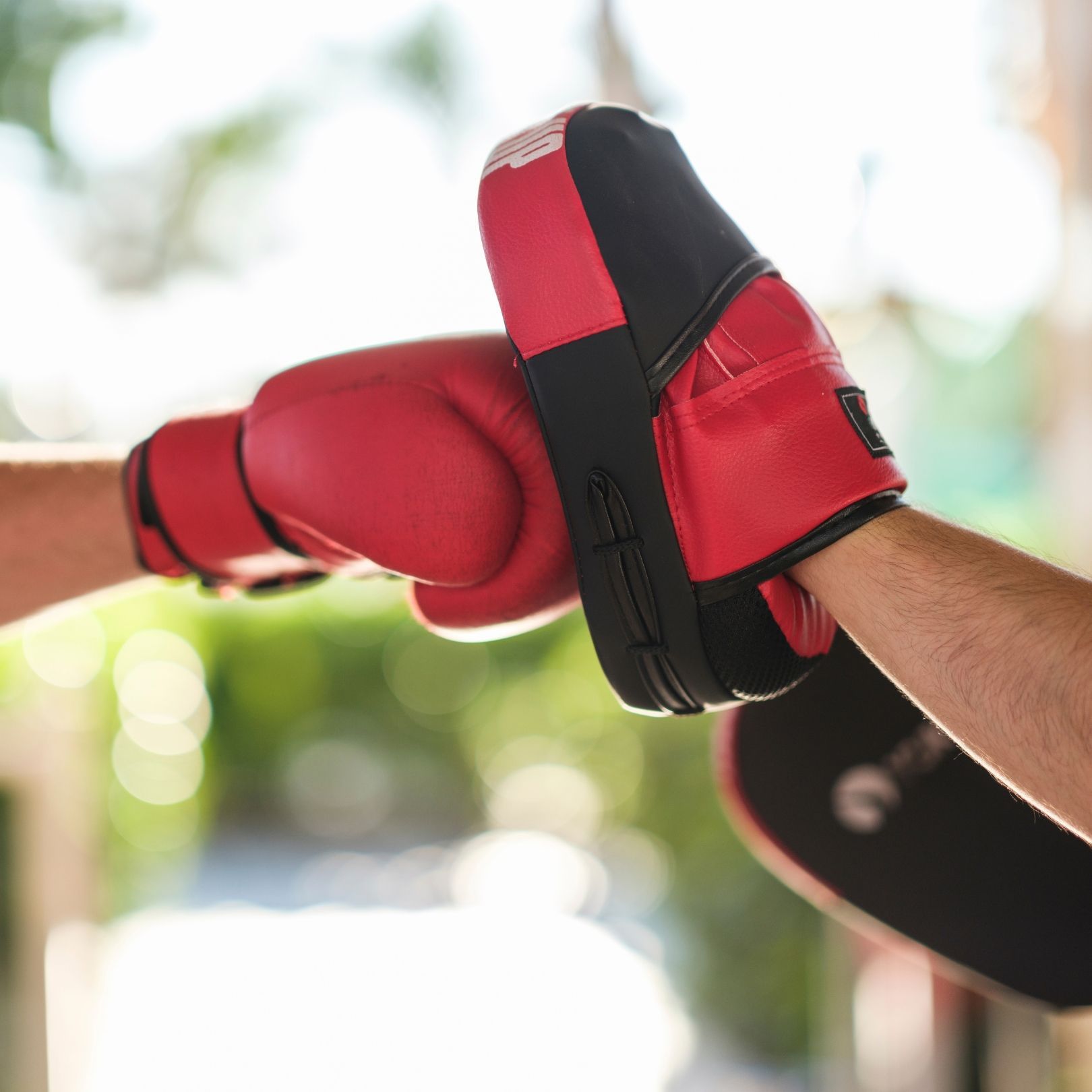 A person wears a red boxing glove striking a red and black focus mitt held by another person against a blurred background.