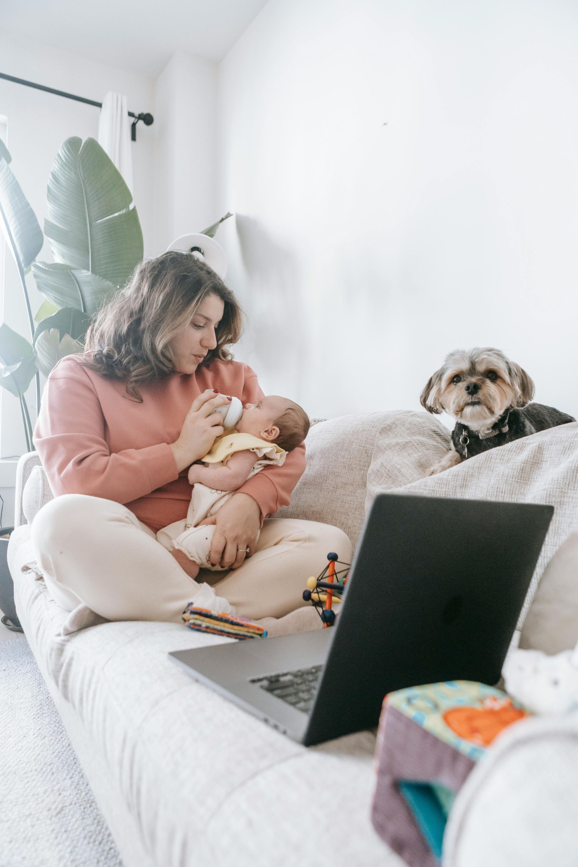 A mom sitting on the couch feeding her newborn while on a virtual one-on-one postpartum doula support call.