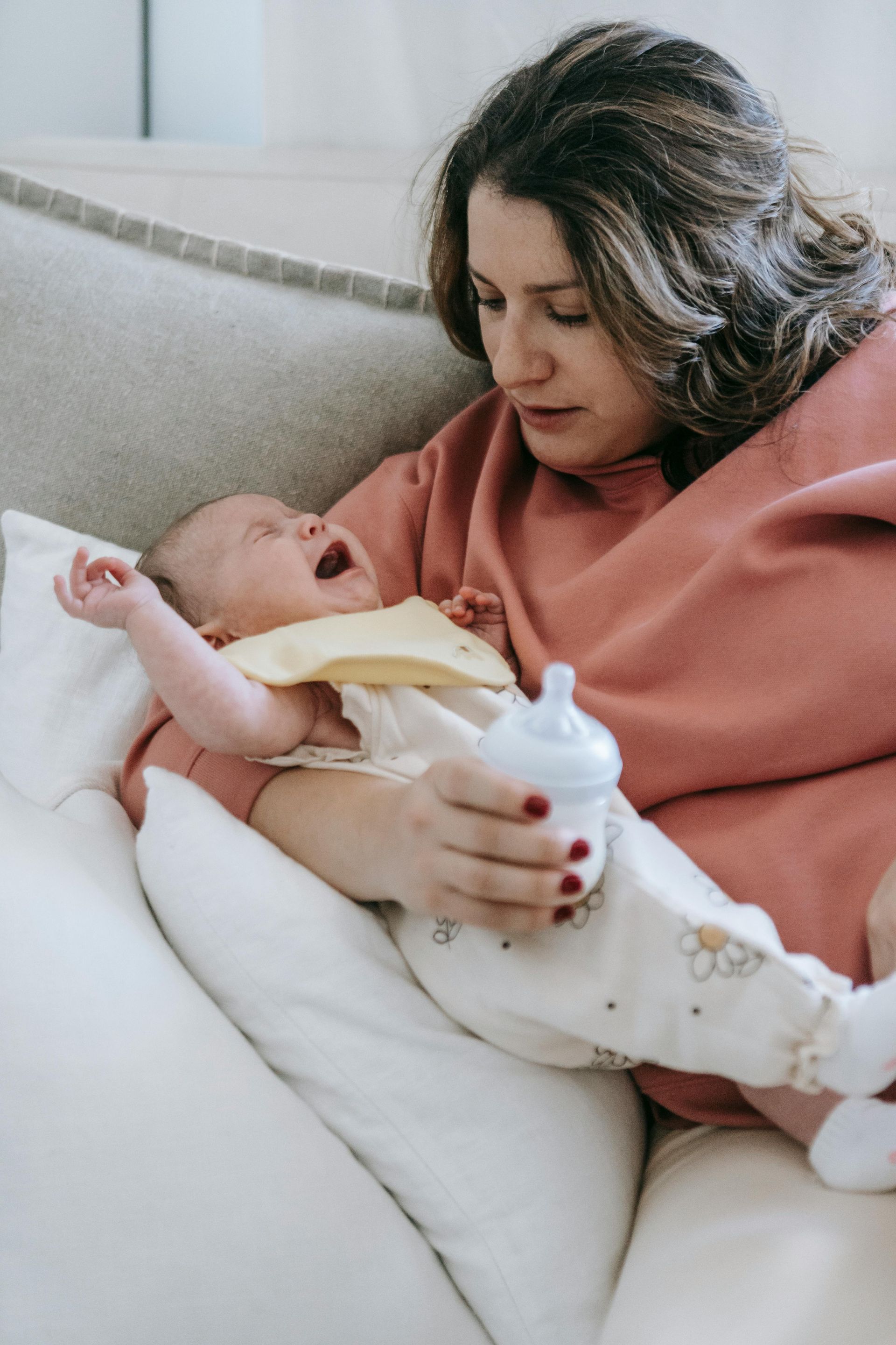 A tired mother holding a crying newborn, sitting in a cozy living room, symbolizing the challenges o