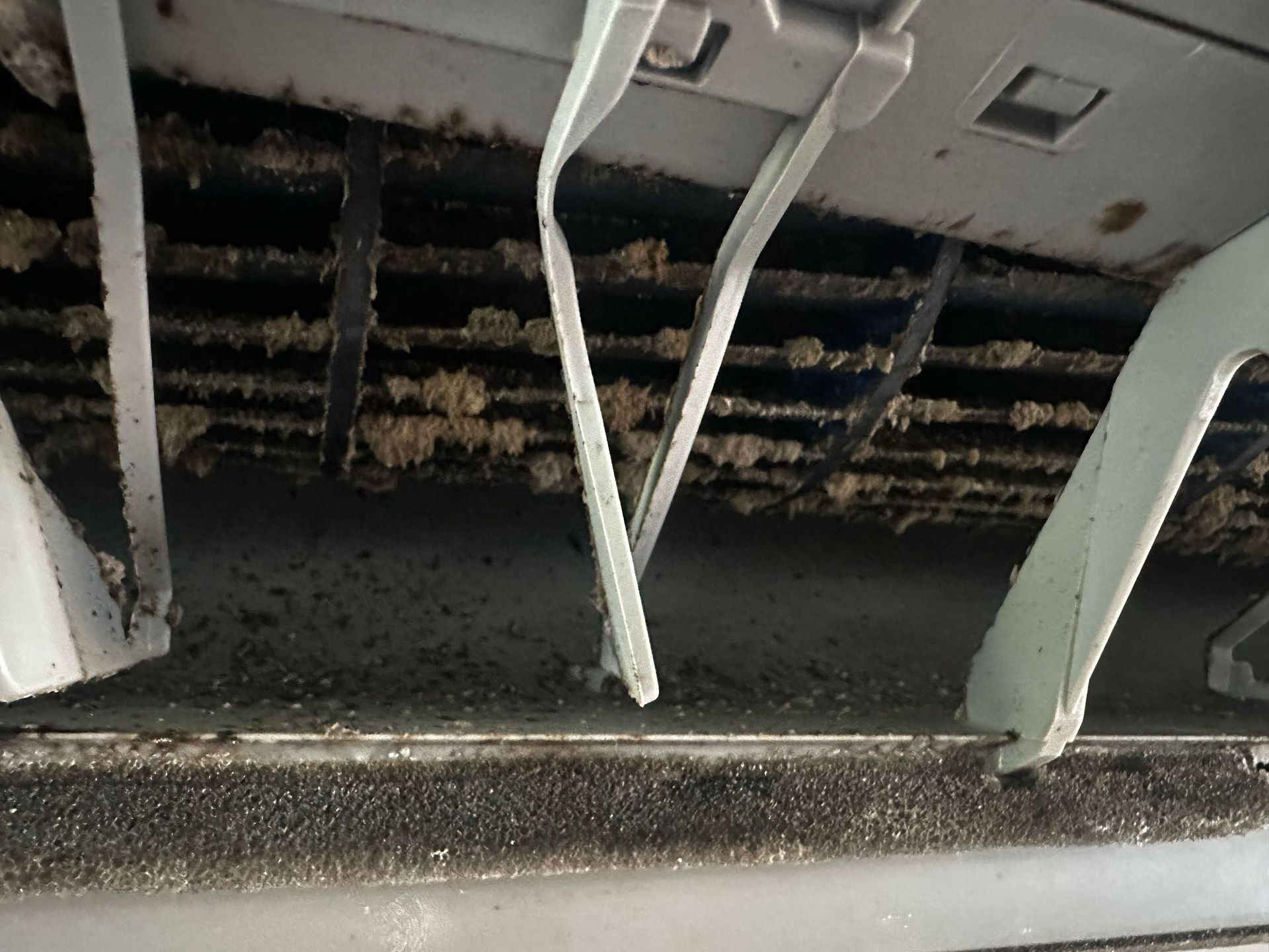 Grille d'aération de climatiseur sale, avec de la poussière et des débris visibles sur les pales et les zones environnantes.