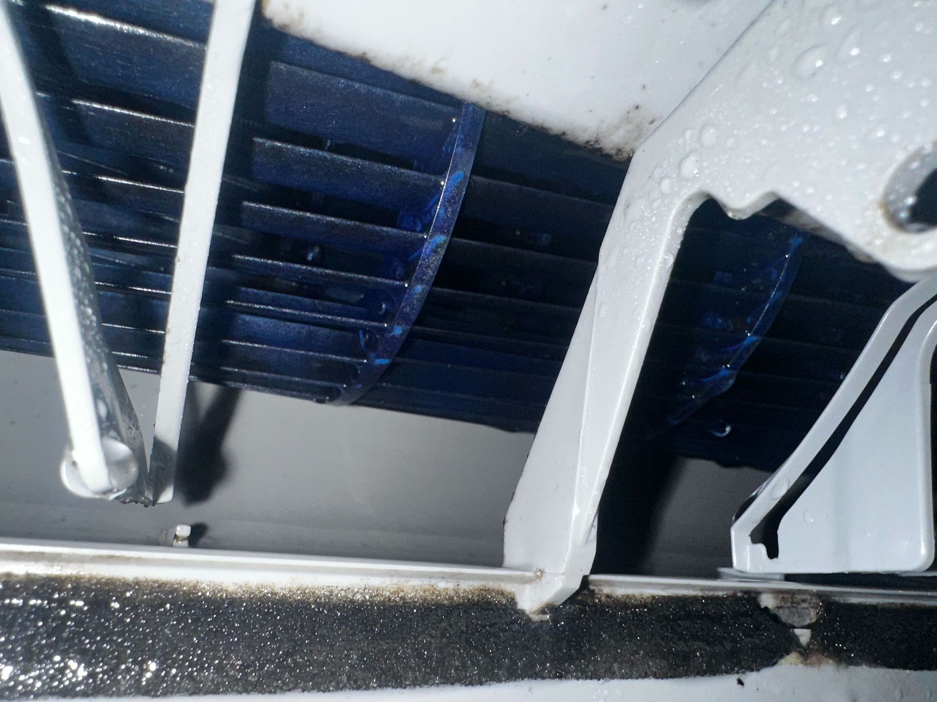 Intérieur d'un climatiseur : ailettes de refroidissement bleues, cadre métallique blanc avec des gouttelettes d'eau.