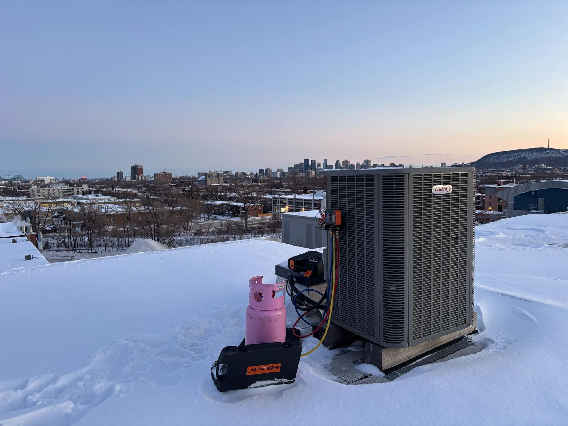 Unité de climatisation sur un toit enneigé; réservoir de réfrigérant rose, outils présents.