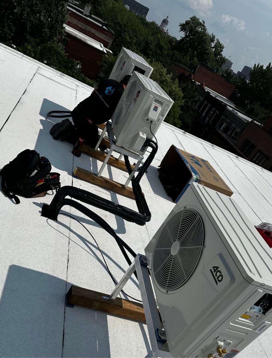 Des techniciens en CVC installent des unités de climatisation sur un toit blanc.