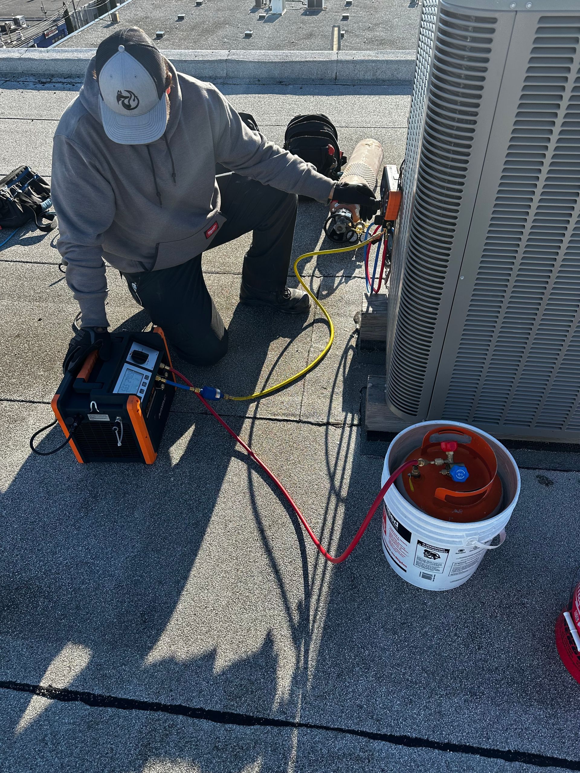 Un technicien en climatisation travaille sur une unité de climatisation sur le toit. Il est en train de raccorder des tuyaux, avec le réservoir et l'équipement.