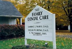 A white sign for a family dental care is in front of a house.