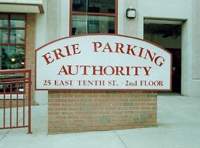 A sign for the erie parking authority is on the sidewalk in front of a building.