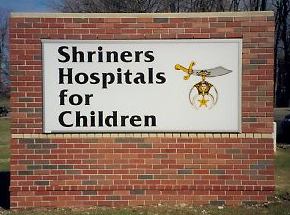 A sign for shriners hospitals for children is on a brick wall.