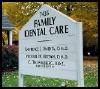 A white sign for family dental care is sitting in the grass.