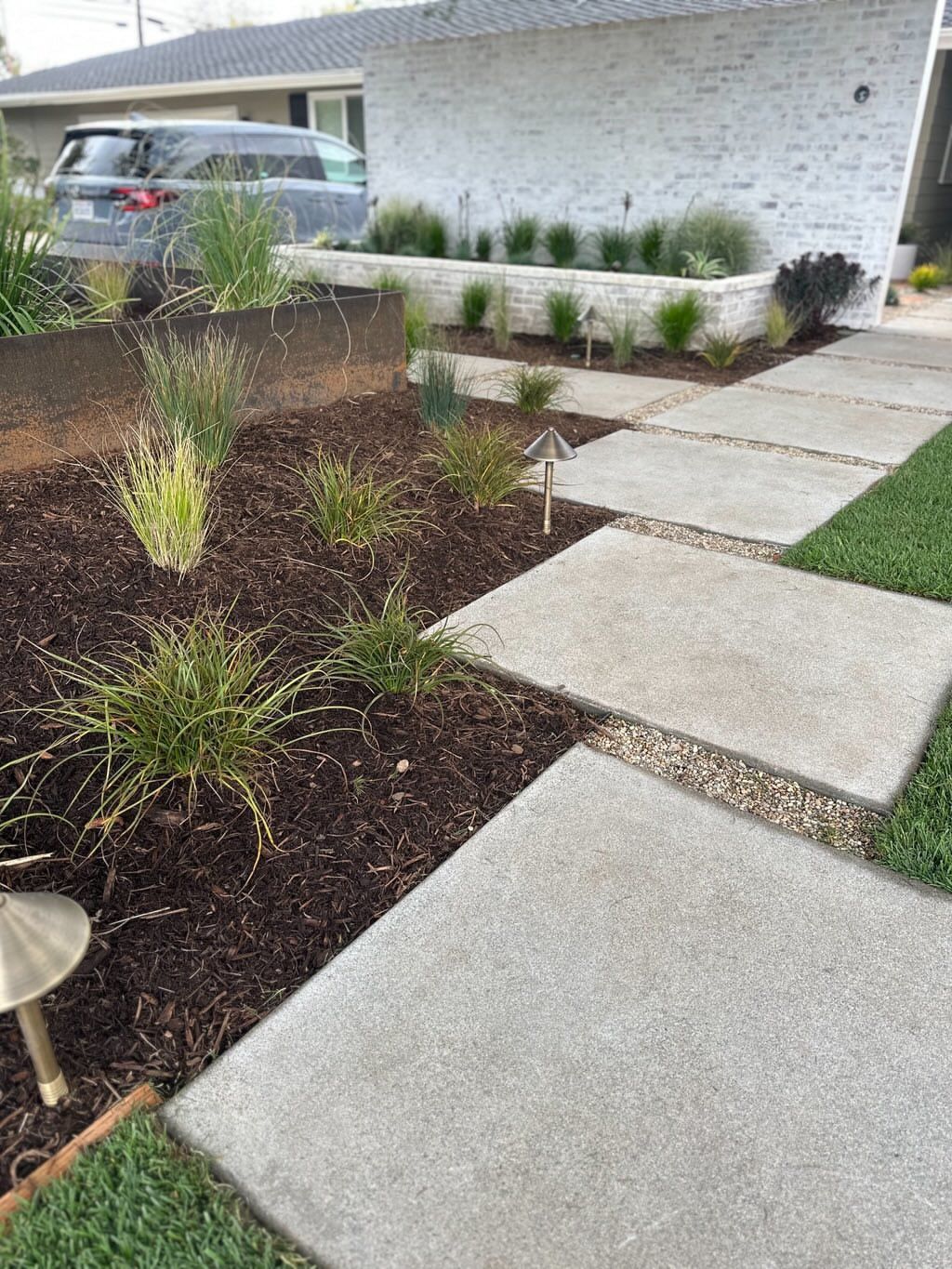 A concrete walkway leading to a house with a car parked in front of it.