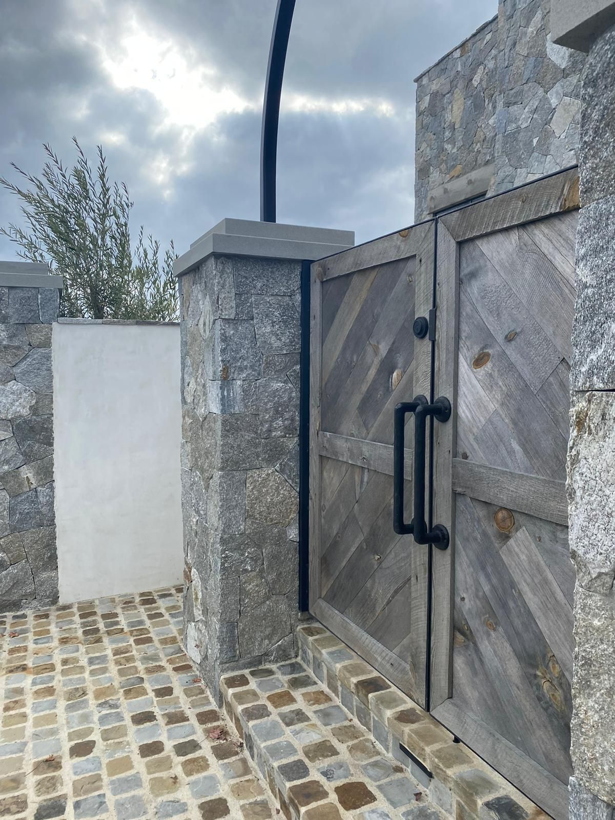 A wooden gate with a black handle is between two stone pillars.
