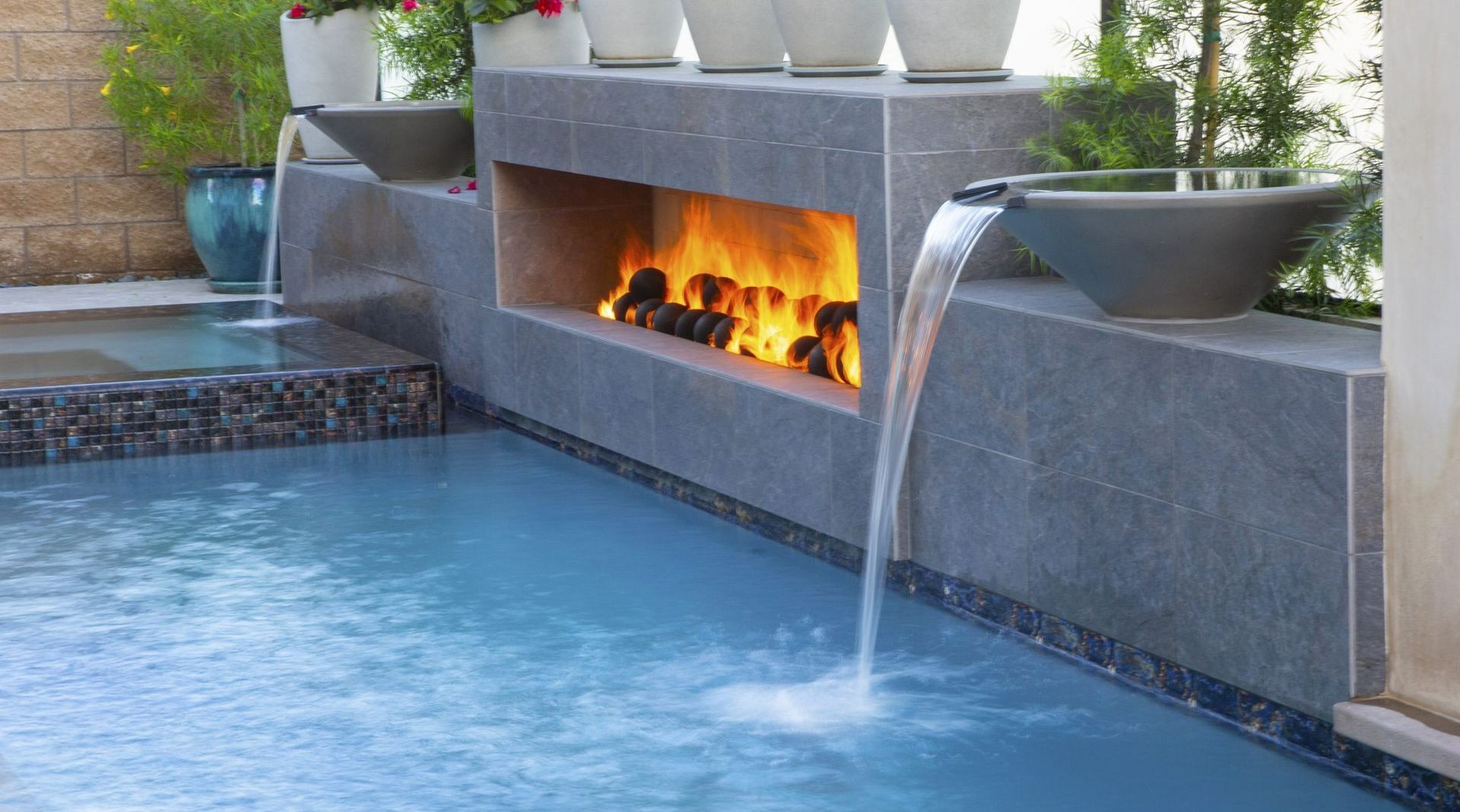A pool with a waterfall and a fireplace in the background.