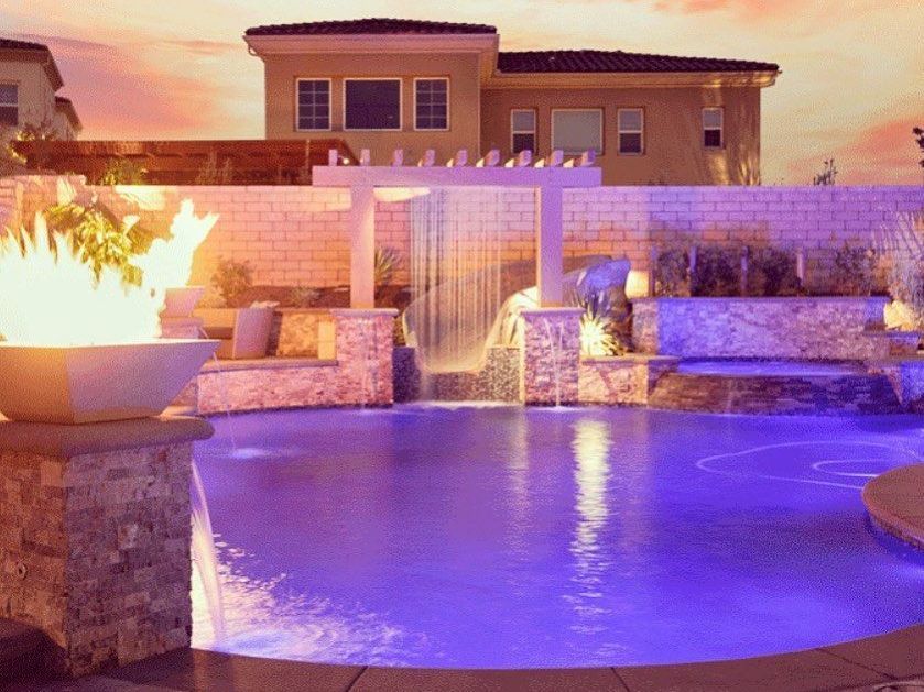 A large swimming pool with a waterfall and a fire pit