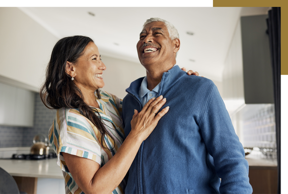 A woman is hugging an older man in a kitchen.