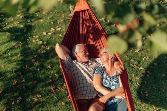 An elderly couple is laying in a hammock in the grass.