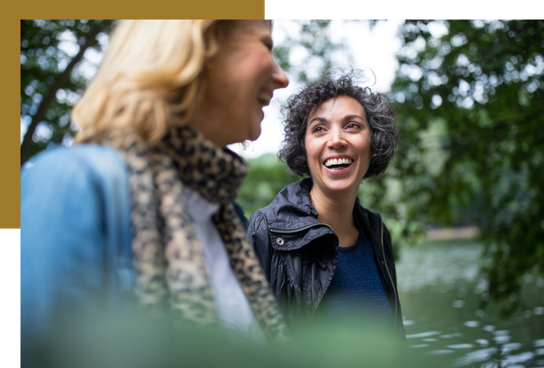 Two women are standing next to each other in front of a lake and smiling.