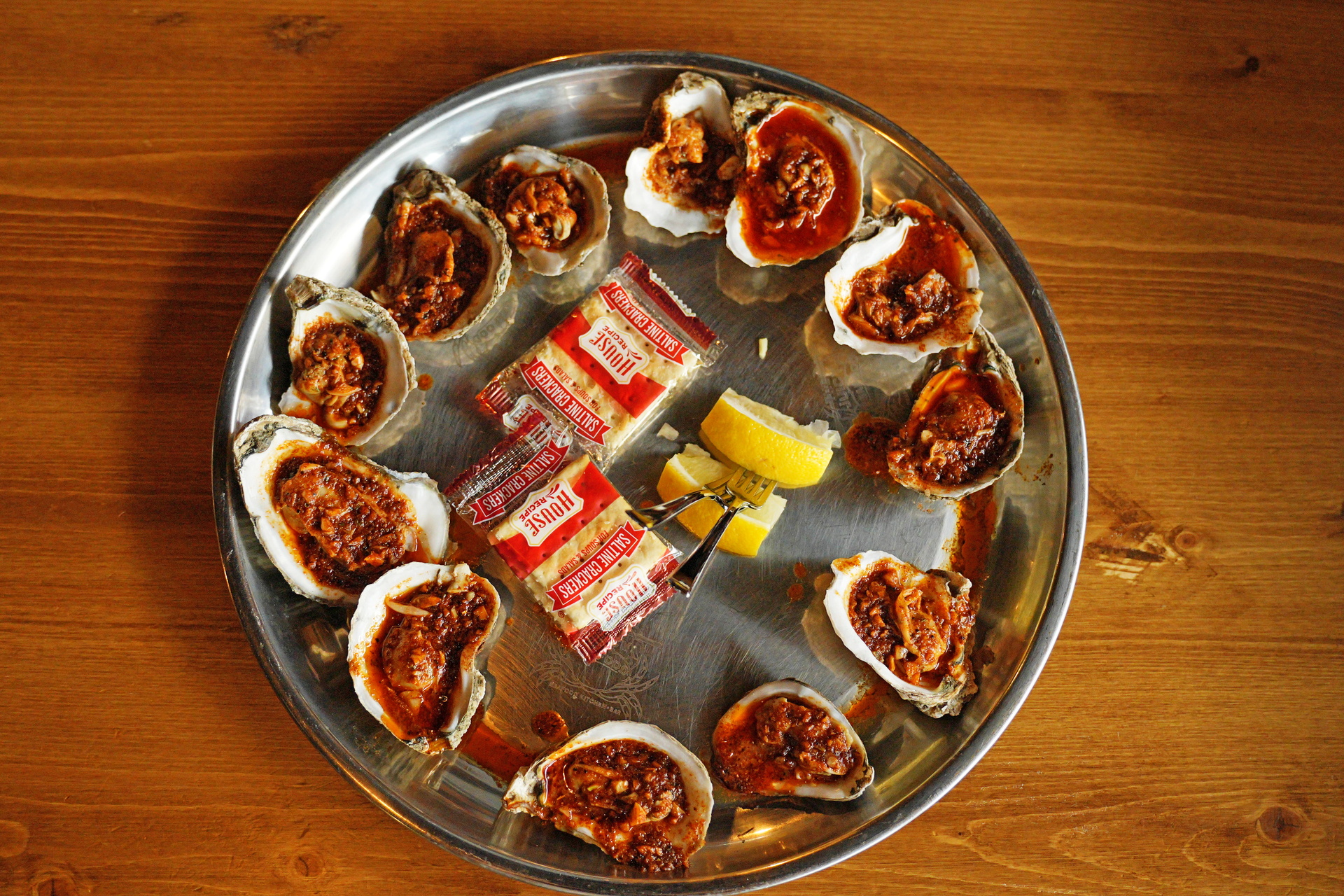A plate of oysters with sauce and lemon on a wooden table.