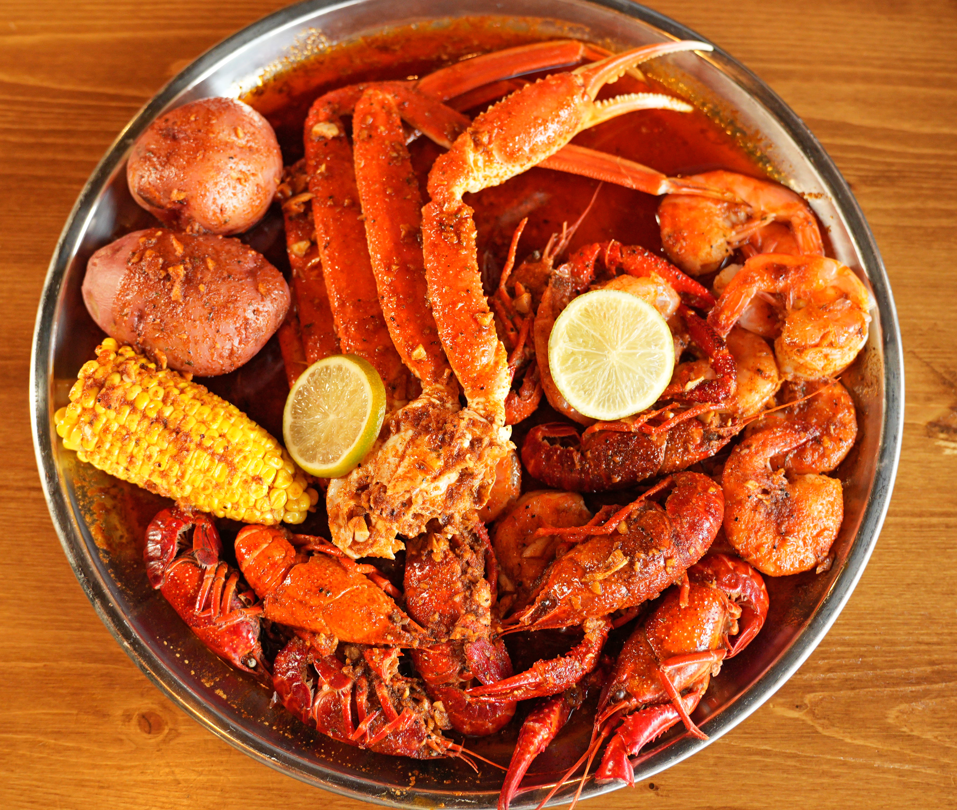 A plate of crab legs , shrimp , corn on the cob and potatoes on a wooden table.