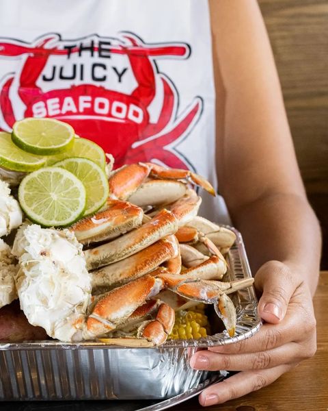 A person is holding a tray of crab legs and corn on the cob.