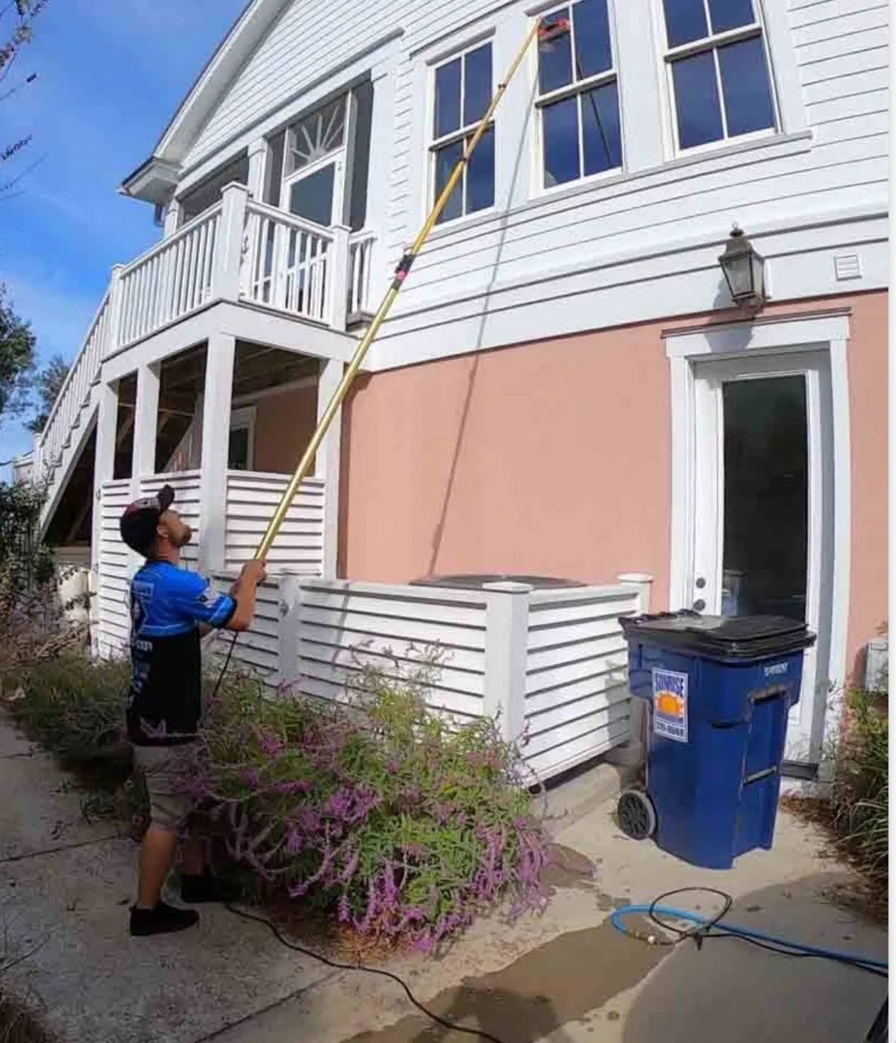 A man is cleaning the windows of a house with a hose.