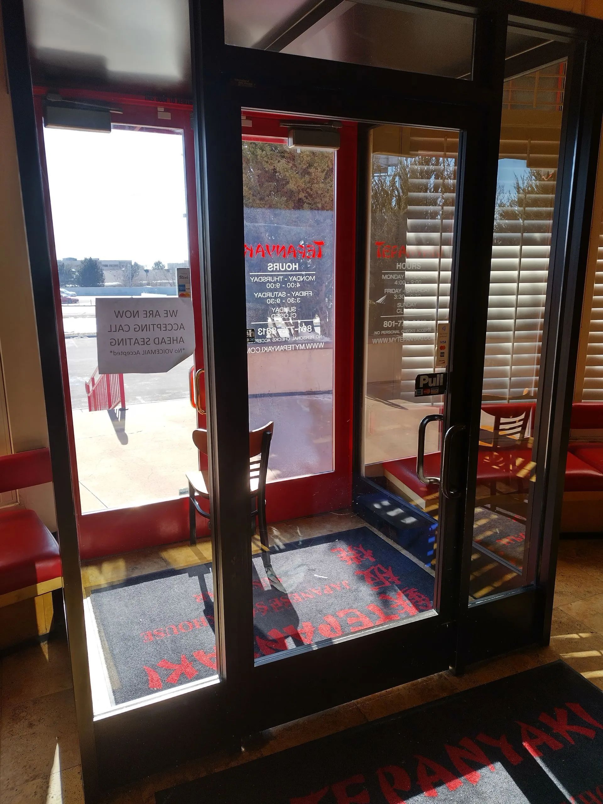 A restaurant with a red door and a black mat on the floor.