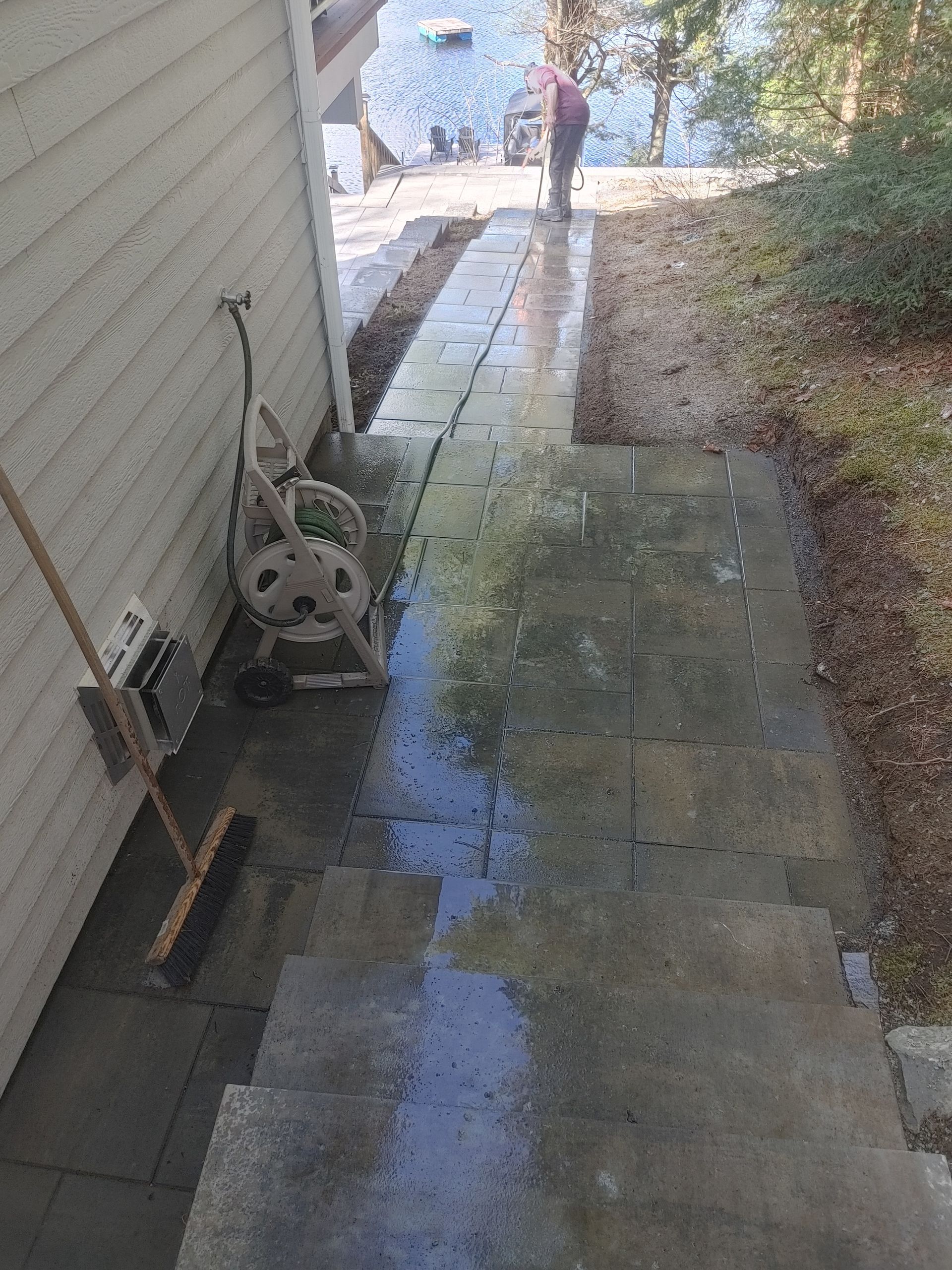 Marches et allée en béton mouillées menant à l'eau, personne arrosant avec un tuyau d'arrosage.