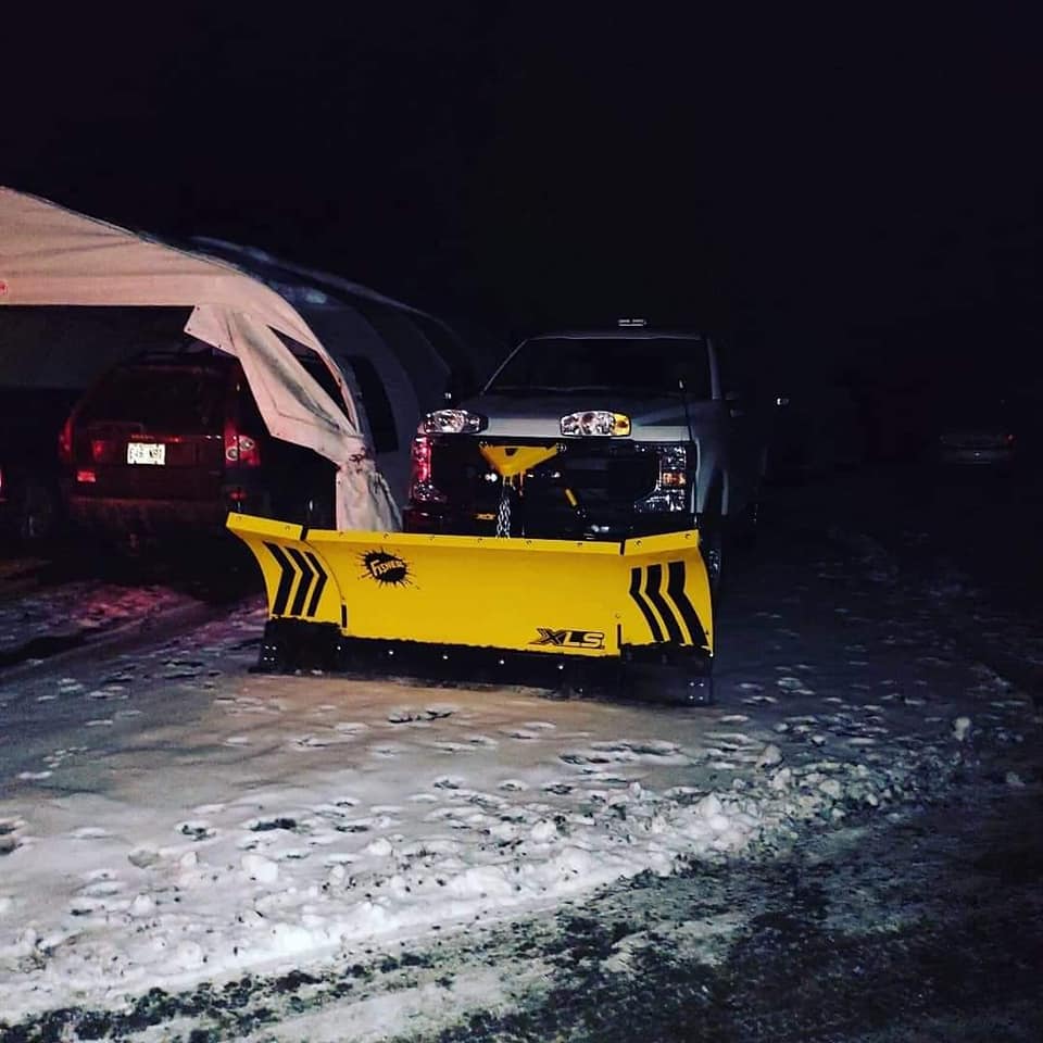 Un camion équipé d'une lame à neige jaune vif déneige la nuit.