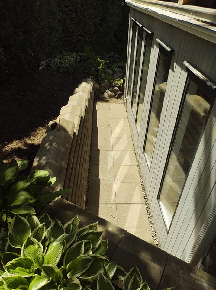 Bâtiment gris avec de hautes fenêtres et une terrasse en béton jouxtant un mur de soutènement et des plantes.