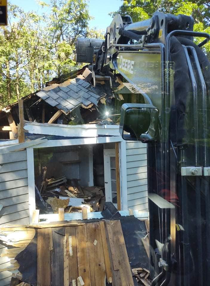 Démolition d'une maison. Le bras d'une excavatrice démolit un bâtiment aux poutres et au bardage apparents.