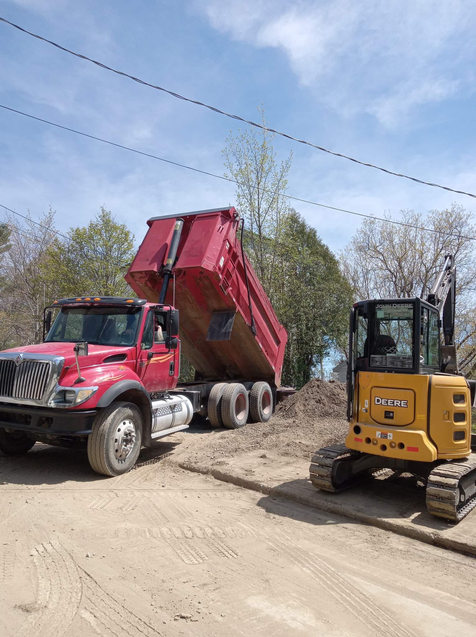 Camion-benne rouge déchargeant de la terre, pelleteuse jaune à proximité. Chantier.